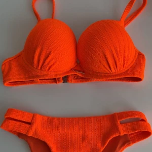 Orange ribbad bikini  - Snygg orange bikini med ribbad struktur och vadderade kupor som ger en push up effekt. Överdelen har justerbara axelband och metallspänne bak. Underdelen har dubbla band i sidorna för en cool detalj. Perfekt för stranden eller poolen. Har aldrig använt den då jag inte tycker om underdelen eller färgen på mig. Ord pris 399kr, pris kan diskuteras.