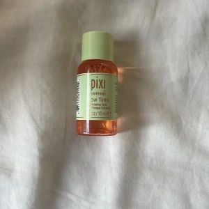 Pixi Glow Tonic Exfolierande Toner - Pixi Glow Tonic är en exfolierande toner i en smidig 15 ml plastflaska med mintgrönt lock och etikett. Innehållet är orangefärgat och passar perfekt för att ge huden extra glow och fräschör. Perfekt att ha med i väskan eller på resan. Aldrig använd!