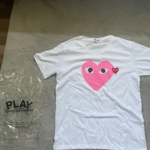 Vit Comme des Garçons Play t-shirt - Säljer denna vita Comme des Garçons Play med ett rosa hjärta! Den är i nyskick och endast använd 1-2 gånger. Priset är inte hugget i sten så kom med bud! Tar även emot intressanta byten!