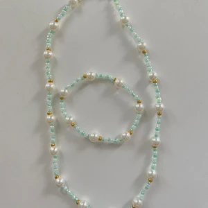 Pärlhalsband och armband i mintgrönt - Snyggt set med halsband och armband av små mintgröna pärlor, vita pärlor och små guldfärgade detaljer. Perfekt för att ge din outfit en fräsch och trendig touch. Pärlorna är runda och sitter på elastisk tråd för enkel användning.