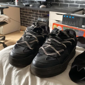 Chunky svarta sneakers från Bershka - Chunky svarta sneakers från Bershka med bred, kraftig sula och svart-vita mönstrade snören. Ovandelen är i syntetmaterial med mesh-detaljer för extra andningsförmåga. Snygg streetstil som passar perfekt till jeans eller cargo.