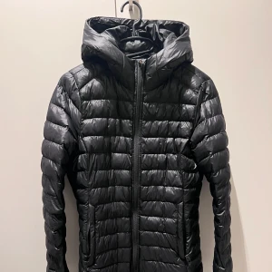 Everest - Svart pufferjacka med huva - Säljer en svart pufferjacka med huva och dragkedja hela vägen. Jackan har quiltad design och två fickor på sidorna. Perfekt för kyliga dagar och riktigt skön att bära. Sitter normalt