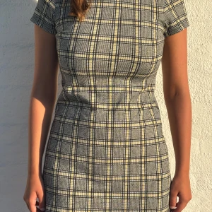 Rutig kortklänning från Divided - Trendig kortklänning i svart, vitt och gult från Divided (H&M) med stretchigt tyg och figurnära passform. Korta ärmar, rund hals och cool dragkedja med ring bak. Perfekt för en vardagslook med edge eller som en partyklänning 🐝  📏 Storlek: 38/M 🧺 Mjukt, stretchigt tyg – superskön! 📬 Skickas snabbt