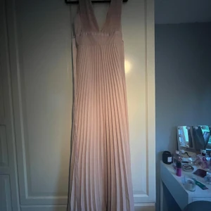 Ljusrosa långklänning - Supersnygg ljusrosa långklänning med djup v-ringning och snörad midja. Perfekt för bal eller student! Endast använd 1 gång på min bal. Jag är 164cm och hade klackar på min bal, den är även lite uppsydd så går att få den längre.