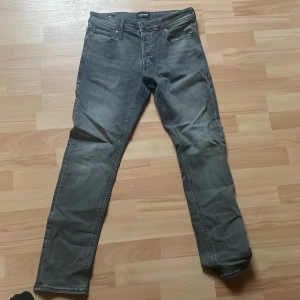 Grå slim jeans Jack & Jones 29/30 - Snygga grå jeans från Jack & Jones, modell Slim/Glenn. De har en slim passform och klassisk femficksdesign. Jeansen är i stretchigt material för extra komfort och har en snygg tvättad look. Perfekta för dig som gillar en smal siluett och stilren vibe.