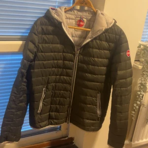 Olivgrön Colmar pufferjacka med huva - Säljer en  vintage olivgrön pufferjacka från Colmar med huva och snygga detaljer. Jackan har quiltad design, dragkedja framtill och två fickor med dragkedja. Perfekt för kyliga dagar och har en clean look med Colmar-logga på ärmen. Jackan har en liten defekt vid sömnen på vänstra armen. Tveka inte på att höra av dig 