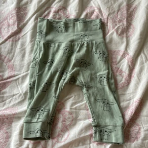 Gröna Star Wars babybyxor H&M strl 62 - Söta ljusgröna babybyxor från H&M med Baby Yoda-motiv från Star Wars. Byxorna är i mjuk ekologisk bomull och har bred mudd i midjan för extra komfort. Perfekta för små Star Wars-fans!