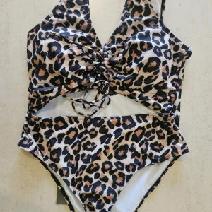 Leopardmönstrad baddräkt med snörning - Snygg baddräkt i leopardmönster med coola cut-outs och snörning framtill. Färgerna går i svart, beige och brunt. Tillverkad i stretchig polyesterblandning som sitter skönt på kroppen. Perfekt för dig som vill sticka ut på stranden!