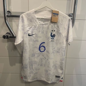 Frankrike Pogba fotbollströja säsong 22/23 away shirt player version  - Snygg vit Frankrike fotbollströja från Nike med Pogba och nummer 6 i blått. Tröjan är från säsongen 22/23 och är en playerversion som innebär att den är lite mindre i passform då det är de tröjorna spelarna kör med. Den är i princip helt ny bara testad en gång. Har fortfarande lappen kvar. Pris går att diskutera  