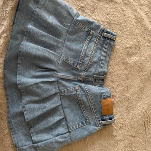 Jeanskjol från Weekday, ljusblå - Säljer en ljusblå jeanskjol från Weekday med klassisk femficksdesign och veckad nederdel. Kjolen är kort och har bälteshällor samt knappar framtill. Perfekt för dig som gillar en avslappnad och trendig stil. SYTT SJÄLV!