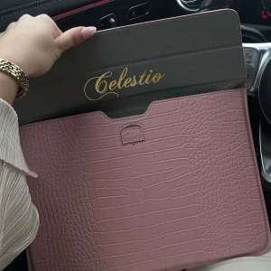 Rosa datorväska från Celestio - Snygg datorväska i ljusrosa från Celestio med croco-mönstrad yta. Väskan har ett stilrent och modernt fodralformat med magnetisk stängning och plats för laptop eller surfplatta. Perfekt accessoar för att lyfta din tech-stil.