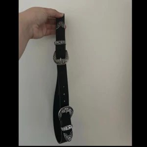 bälte med silverdetaljer - Snyggt svart bälte i skinn med detaljerade silverspännen och mönstrade metalldelar i westernstil. Perfekt accessoar för att lyfta din outfit med en cool touch. Bältet har flera hål för justerbar passform.
