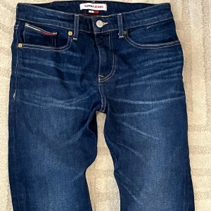 Tommy Jeans jeans 30/32 - Mörkblå jeans från Tommy Jeans med klassisk femficksdesign, kontrastsömmar och läderpatch bak i midjan. Snygga detaljer som logga på bakfickan och rödvit detalj vid myntfickan. Perfekta för dig som gillar stilrena och tidlösa jeans.