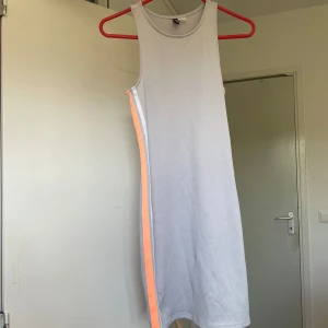 Sportig klänning - Grå ribbad klänning med ärmlös design och rund hals. Klänningen har en orange rand längs sidan som ger en sportig vibe. Mjuk och bekväm. Perfekt för varma dagar och enkel att styla med sneakers eller sandaler.