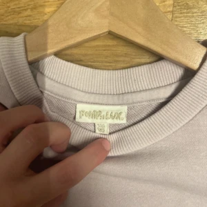 Ljuslila tröja POMP de LUX - Ljuslila tröja från POMP de LUX med texten 'Blossom Poetry' i guld på ryggen. Tröjan har rund halsringning och puffiga trekvartsärmar med resår vid ärmslut. Perfekt för dig som gillar en söt och stilren look.