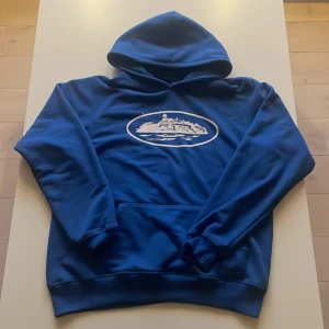 Blå hoodie från Corteiz - Blå Corteiz hoodie  Clean hoodie från hypade Corteiz i snygg blå färg. Mjuk bomull, skön passform och streetwear-vibe rakt igenom. Perfekt till både vardag och outfit pics. Bra skick. Storlek: medium men är lite stor så skulle säga i mitten av M och L. Priset är inte hugget i sten så det är bara att buda😘