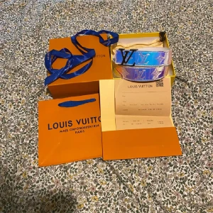 Louis Vuitton holografiskt bälte - Säljer ett sjukt snyggt Louis Vuitton bälte i holografiskt skinn med ikoniska LV-loggor och silverfärgat spänne. Bältet har en bred design och reflekterar olika färger beroende på ljuset. Kommer med originalbox, dustbag och kvitto.