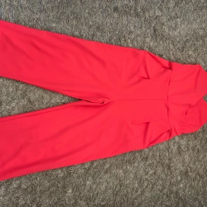 Rosa byxdress med smala axelband - Snygg rosa byxdress med smala axelband och markerad midja. Vida ben och enkel, stilren design som ger en cool vibe. Perfekt för dig som vill sticka ut med färg och ha något bekvämt men ändå trendigt. Materialet känns mjukt och följsamt.