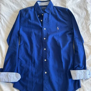 Ralph Lauren Skjorta - Säljer denna fina och stiliga ralph lauren skjorta. Färgen är blå med randiga detaljer i färg ljusblå & vit. Perfekt look till både sommaren och våren! Använd 1-2 gånger dvs ny! Storlek S och är i custom fit. Hör av dig vid funderingar!