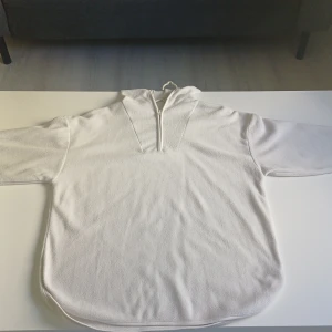 Vit fleecehoodie från 157, strl S - Mysig vit hoodie från 157 i fleece med half zip och huva. Perfekt för kyliga dagar, enkel och stilren design. Modellen är loose fit med långa ärmar och dragsko nertill. Passar dig som gillar bekväma och avslappnade plagg.