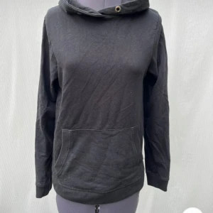 Svart hoodie från OTP Leisurewear - En svart hoodie från OTP Leisurewear i storlek S. Tröjan har huva med metallöljetter, magficka och långa ärmar. Enkel och stilren design som passar perfekt till chill dagar. Tillverkad i mjuk bomull för skön känsla.