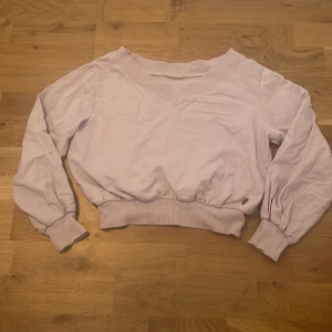 Ljuslila sweatshirt från Rükie - Ljuslila sweatshirt från Rükie med broderad logga på bröstet. Tröjan har v-ringad hals, breda muddar i ärmslut och midja samt långärmad passform. Mjuk bomullskänsla och avslappnad look, perfekt till jeans eller kjol.