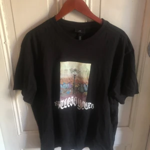 Svart t-shirt med grafiskt tryck H&M - Svart t-shirt från H&M med coolt grafiskt tryck framtill som föreställer graffiti och texten 'Restless Youth' i vit stiliserad font. Klassisk passform med rund hals och korta ärmar. Perfekt för dig som gillar streetstyle och vill sticka ut.
