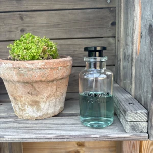 Louis Vuitton Imagination parfym - Exklusiv parfym från Louis Vuitton, Imagination, i en stilren genomskinlig glasflaska med ljusblå vätska. Flaskan har svart rund kork med LV-logga på toppen och minimalistisk text framtill. Perfekt för dig som gillar lyxiga dofter och snygg design.