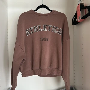 Brun oversized sweatshirt ATHLETICS - Säljer en brun oversized sweatshirt med trycket 'ATHLETICS 1998' på framsidan . Materialet känns som mjuk bomullsmix.