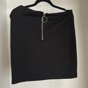 Svart kortkjol med dragkedja - Svart enkel kortkjol med rak passform och en snygg silverfärgad dragkedja framtill med rund detalj. Materialet känns mjukt och stretchigt.
