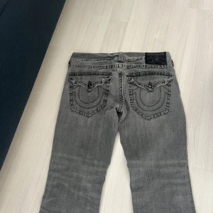 Grå True Religion Ricky jeans - Säljer ett par grå jeans från True Religion, modell Ricky. Jeansen har klassiska kontrastsömmar, snygga bakfickor med lock och knappar samt en cool tvättad look. Tillverkade i bomull med dragkedja och knapp framtill. Funkar för L och M ifall man är lång jag är själv 170 och dom passar perfekt säljer dom eftersom dom inte längre passar i midjan  .Dom är vinted köpta i london 💞