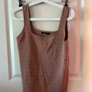 Randig brun linnetopp från H&M - Säljer en brun linnetopp från H&M med tunna orangea ränder. Toppen är ärmlös med breda axelband och har en rak, enkel passform. Perfekt för varma dagar och enkel att matcha med jeans eller shorts.
