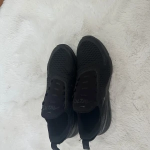 Svarta Nike Air Max 270 sneakers - Snygga helsvarta Nike Air Max 270 sneakers med mesh-ovandel och tydlig Air Max-dämpning i hälen. Skorna har en sportig vibe, diskreta loggor och en chunky sula som ger extra komfort. Perfekta för dig som gillar streetstyle och vill ha en clean look.