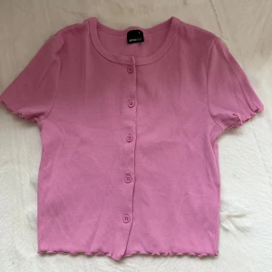 Rosa ribbad topp från Gina Tricot - Supersöt rosa topp från Gina Tricot med korta ärmar och knappar framtill. Modellen är croppad med vågig kant nertill och i ärmslut.