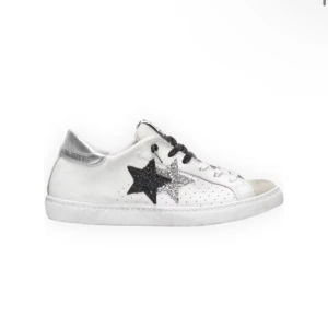 Vita sneakers med glittriga stjärnor - Snygga vita sneakers med svarta och silverglittriga stjärnor på sidan. Skorna har svarta och vita snören, perforerade detaljer och en metallic-silver häl. Perfekt för dig som vill sticka ut med coola detaljer.