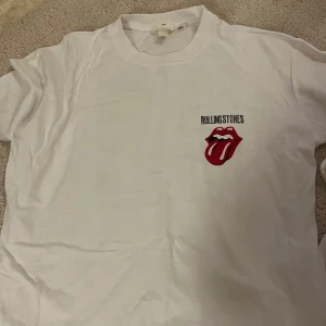 Rolling Stones vit t-shirt H&M - Vit t-shirt från H&M med Rolling Stones-tryck fram och stor konsertgrafik på ryggen. Klassisk crewneck, korta ärmar och ikonisk röd tunga-logga. Perfekt för dig som gillar bandmerch och vill sticka ut med en retrovibe.