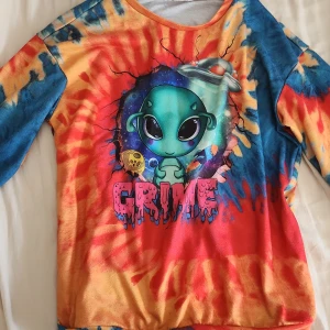 Färgglad tie-dye tröja med alienmotiv - Säljer en långärmad tröja från SHEIN med färgstarkt tie-dye mönster i blått, rött och gult. Framsidan har ett stort tryck med en söt tecknad alien, rymdskepp och texten 'GRIME'. Perfekt för dig som gillar unika och lekfulla plagg. storlek 152 passar xs eller liten s