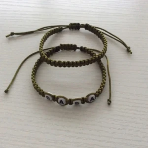 Olivgröna vänskapsarmband med bokstäver  - Två handgjorda olivgröna armband i flätad tråd med justerbar knytning. Det ena armbandet har vita pärlor med svarta bokstäver som bildar ordet 'BABA'. Perfekt accessoar för att ge en personlig touch till din stil. 🎁Extra gåva på köpet.