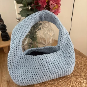 Ljusblå stickad handväska - Superfin ljusblå handväska i stickad design. Väskan har en mjuk och chunky känsla med bred axelrem och rymligt fack. Perfekt för dig som gillar unika accessoarer och vill addera lite färg till din outfit.