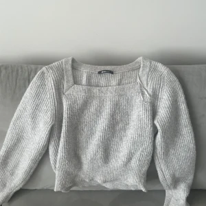 Ljusgrå stickad myströja från Gina Tricot - Supermysig ljusgrå stickad tröja från Gina Tricot med fyrkantig ringning och ribbad struktur. Tröjan har långa ärmar och en något croppad passform som ger en trendig vibe. Perfekt att styla med jeans eller kjol.