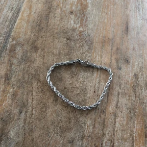 Silverfärgat flätat armband - Snyggt och stilrent armband i silverfärg med flätad design. Perfekt för att ge en elegant touch till din outfit. Lätt att matcha med andra smycken. Den är 20 cm lång. Hör av er vid funderingar 