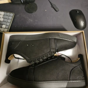 Louboutins - Stilrena svarta sneakers med låg profil och cool röd sula med grafiskt mönster undertill. Skorna har snörning och är tillverkade i textil och syntetmaterial. Perfekta för dig som gillar en clean look med en oväntad detalj under foten.