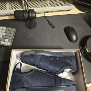Louboutins  - Snygga mörkblå sneakers från Christian Louboutin i mocka med klassisk röd sula och diskret broderad logga på hälen. Skorna har rund tå, platt sula och ton-i-ton snörning. Perfekta för dig som vill ha en stilren och exklusiv look.