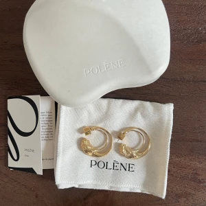 Polène Eroz guldpläterade örhängen - Säljer ett par Polène Eroz hoop örhängen i 24 karat guldplätering. De har en unik, organisk form med både släta och texturerade detaljer. Stiftet har en fyrkantig detalj med Polène-logga. Kommer med originalask och tygpåse.