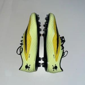 Nike Hypervenom fotbollsskor gul/svart - Säljer ett par Nike Hypervenom fotbollsskor i en riktigt snygg gul och svart färg. Skorna har snörning, mönstrad ovandel och svarta dobbar för gräsplan. Perfekta för dig som vill sticka ut på planen. Skallen på hälen ger extra edge. Jag har 43,5 så dessa passade inte, köpte av en annan och hoppades att de skulle passa men då denna modellen är ”tajtare” och för smala fötter så säljer jag nu vidare dom. Endast provtestade, aldrig använda ute