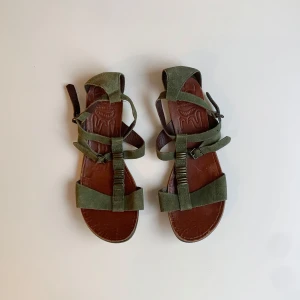 Mocka sandaler från Vagabond - Sandaler från Vagabond i olivgrön mocka med bruna lädersulor. Remmarna har coola metall-detaljer och två justerabara spännen. Sulan har unikt mönster med ansikten och logga.  Priset kan diskuteras☺️
