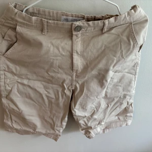 Beige shorts från Zara, stl 164 - Snygga beige shorts från Zara i klassisk modell med knapp och dragkedja framtill. De har två sidofickor och bälteshällor, perfekta för sommardagar. Materialet är mjukt och skönt bomullstyg som andas bra.