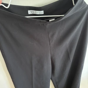 Svarta kostymbyxor från Zara. NYA - Svarta kostymbyxor från Zara med hög midja och raka ben. Byxorna har en stilren look utan synliga detaljer och är gjorda i ett mjukt, vävt material som känns bekvämt. Perfekta för en clean och dressad stil.
