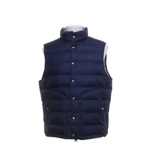 Dunväst från Polo Ralph Lauren - Snygg dunväst från Polo Ralph Lauren med hög krage och tryckknappar. Kan vändas in och ut marinblått och silvergrått med klassisk broderad logga på bröstet. Västen har två stora fickor framtill och quiltad design som ger en sportig vibe.