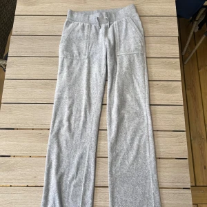 Grå mjukisbyxor Juicy Couture XS - Supermjuka grå mjukisbyxor från Juicy Couture med raka ben, bred resår och snörning i midjan. Fickor fram och bak med knappdetaljer. 